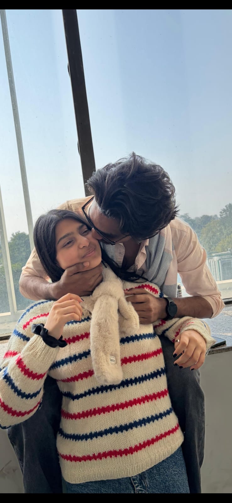 Cheek-kiss in soft daylight — our forever pose.